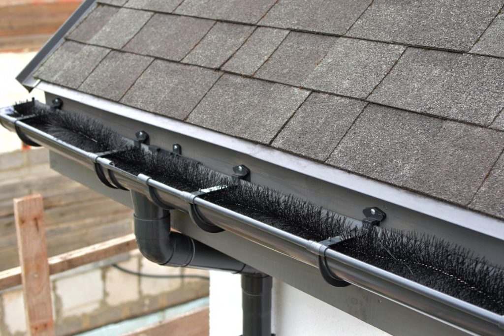 Plastic guard brush in new dark grey plastic rain gutter on asphalt shingles roof